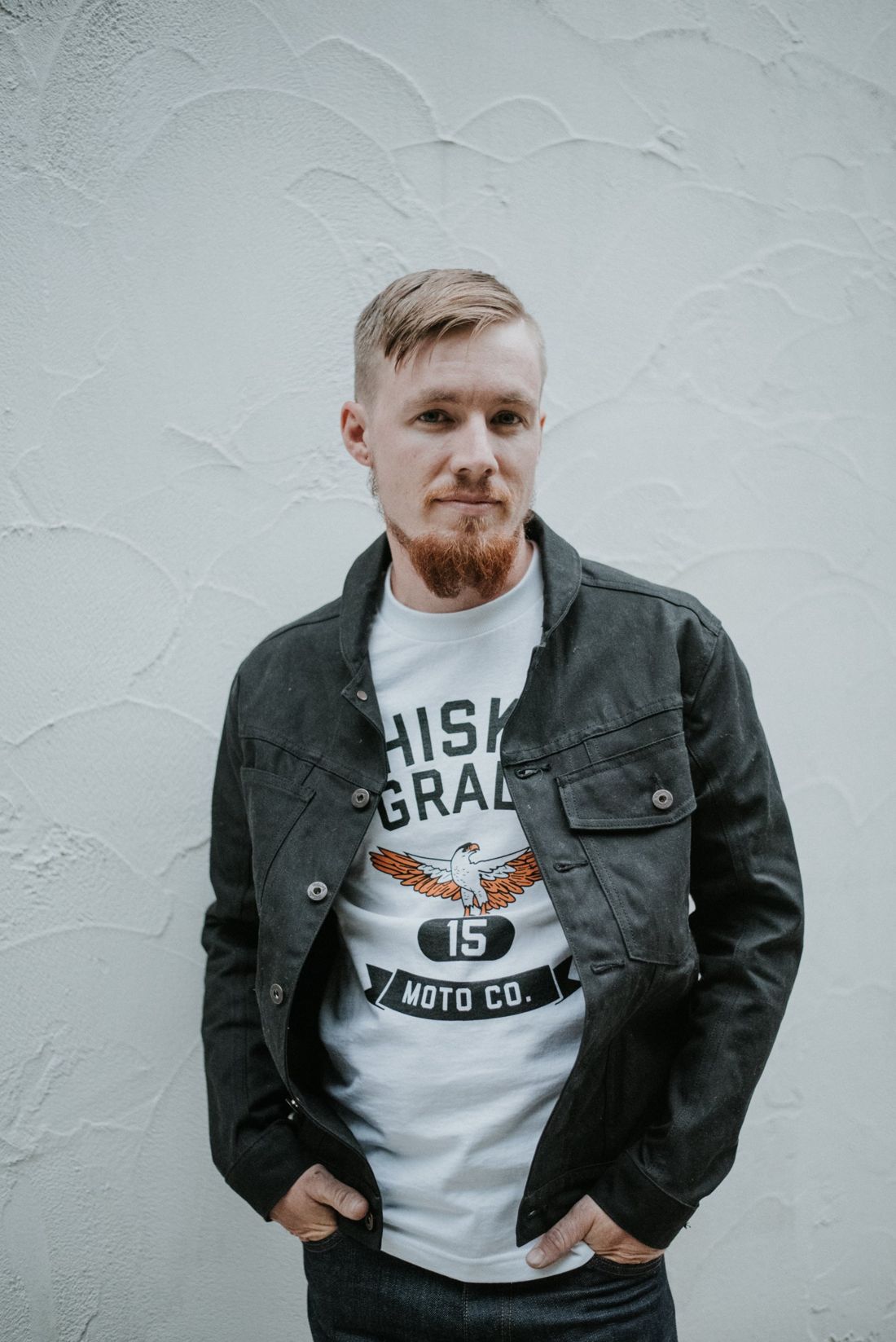 Josh Witt in a black work jacket against a white plaster wall